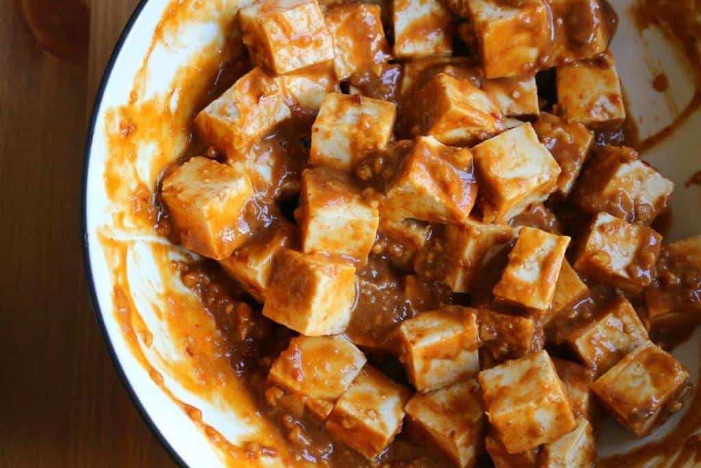 overhead shot of cubed tofu in a bowl tossed with the peanut sauce, ready to be cooked