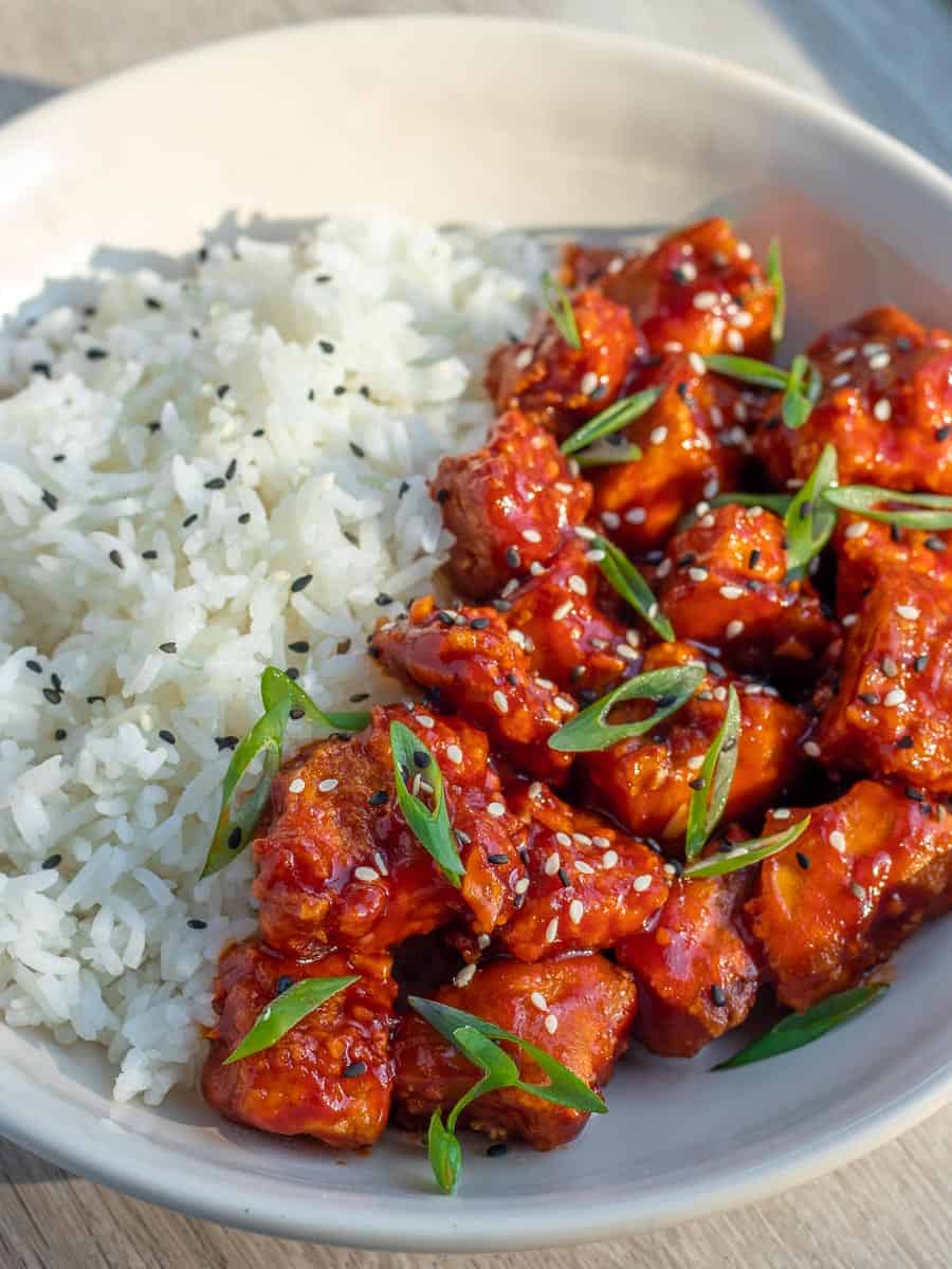 gochujang tofu in a bowl with rice, garnished with scallions and sesame seeds