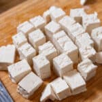 closeup shot of homemade tofu, chopped into cubes on a cutting board
