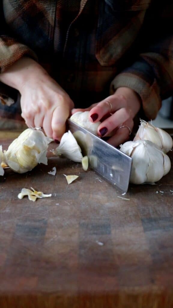 the top of a garlic bulb being chopped off on a cutting board