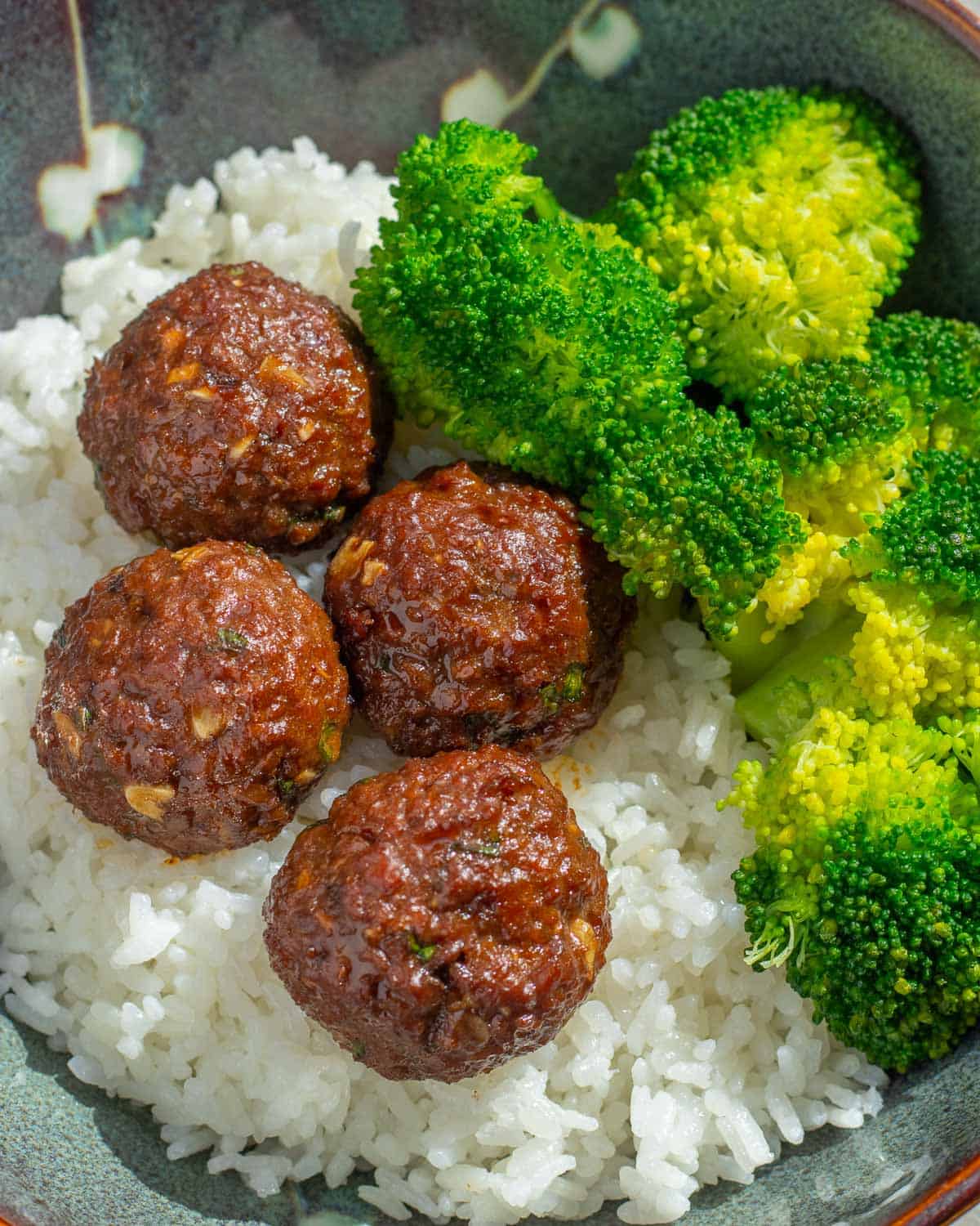 closeup of ginger garlic meatballs in a bowl with rice and broccoli
