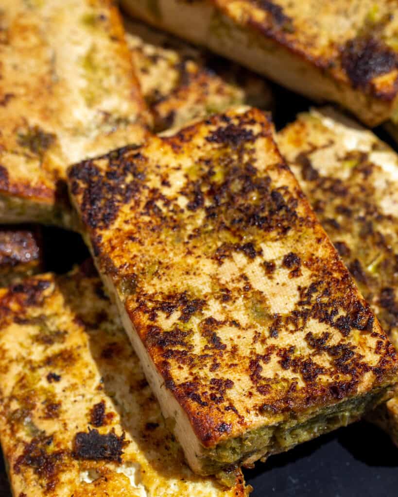 A close up shot of a jerk tofu steak. You can see the greenish marinade on the surface, some of which has turned a crispy golden brown color.