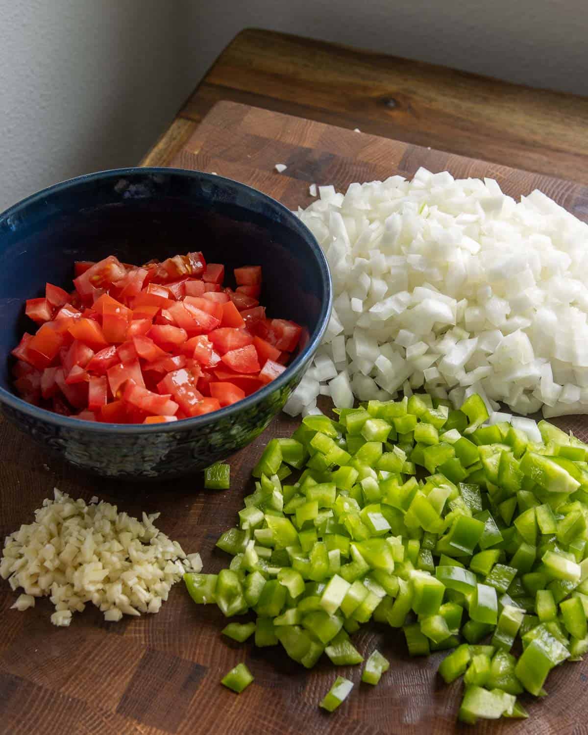 A cutting board with diced ingredients for homemade sofritas, including tomato, onion, pepper and garlic.