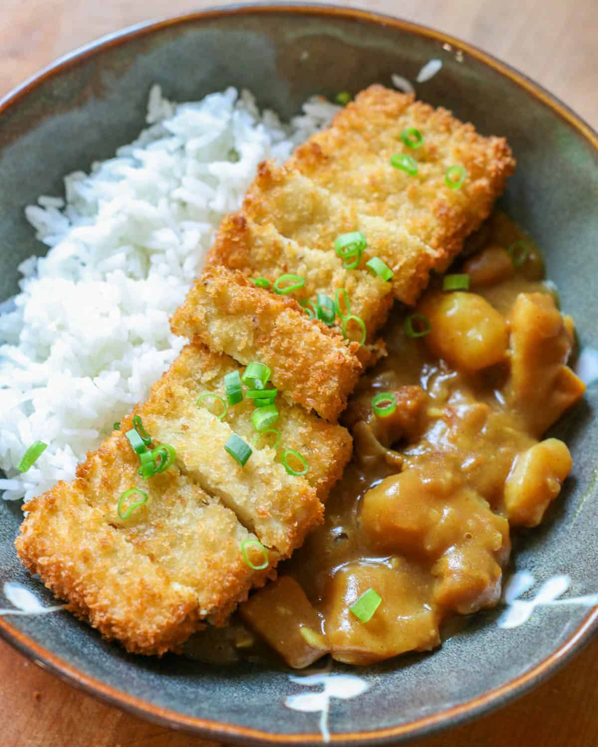 A crispy tofu katsu cutlet, sliced and served with white rice, Japanese curry, topped with scallions.