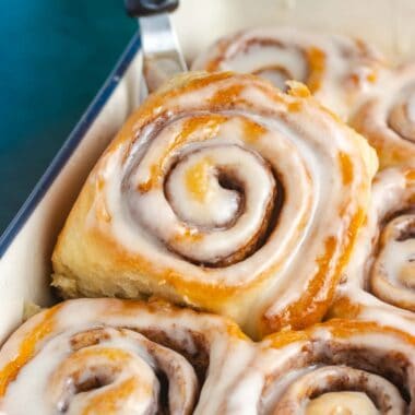 close up of a vegan cinnamon roll being lifted out of a baking pan
