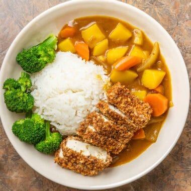 a large white bowl filled with vegan Japanese curry, crispy tofu katsu, white rice, and steamed broccoli